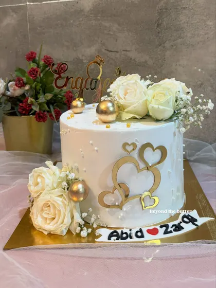 This engagement cake is all about love, featuring golden hearts, fresh white roses, and a custom name banner for the happy couple, Abid and Zarqa.