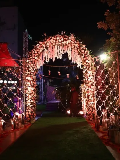 A view down the softly lit walkway leading through the floral arch, with fairy lights on the surrounding bushes enhancing the magical atmosphere.