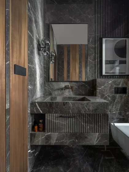 A bathroom for a senior gentleman, designed to be mature and timeless. We used a dark, dramatic marble with strong veining, paired with fluted details and warm walnut wood.