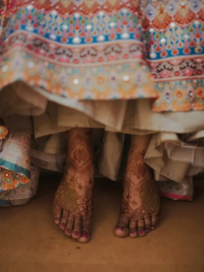 A beautiful detail shot of the bride's feet, adorned with intricate mehndi, peeking out from her lehenga.