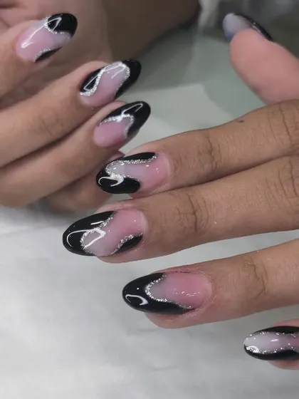 A sleek black and silver glitter swirl design on a sheer nude base. This is a glamorous and edgy look for almond-shaped nails.