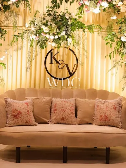 A vintage royal wedding stage. The scalloped sofa, floral printed cushions, and a backdrop of lush flowers and a custom monogram create a look of timeless elegance and personal charm.