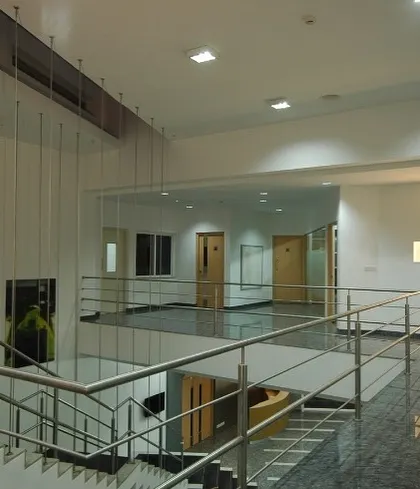 This view of the multi-level interior at Komet India shows how we use open mezzanines and minimalist steel railings to maintain visual connection between floors. This approach fosters a sense of openness and collaboration within the workspace.