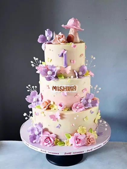 For a magical first birthday, I designed this three-tiered enchanted garden cake. It's adorned with a cascade of hand-sculpted sugar flowers in soft pastel shades, delicate edible butterflies, and a whimsical mushroom house topper. This non-fondant cake shows how elegant and detailed a buttercream finish can be.