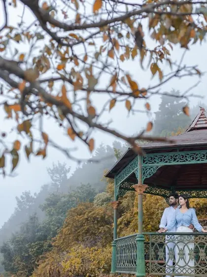 A wide shot showing the couple in the gazebo amidst the misty, atmospheric landscape of Rishikesh. This image captures both the romance of the couple and the beauty of their chosen destination.