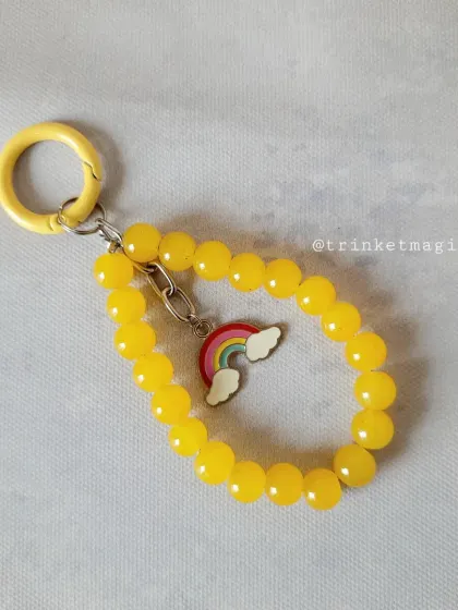 Brighten up your day with this sunny yellow beaded charm. It features a cute rainbow and cloud charm, perfect for adding a cheerful touch to your accessories.