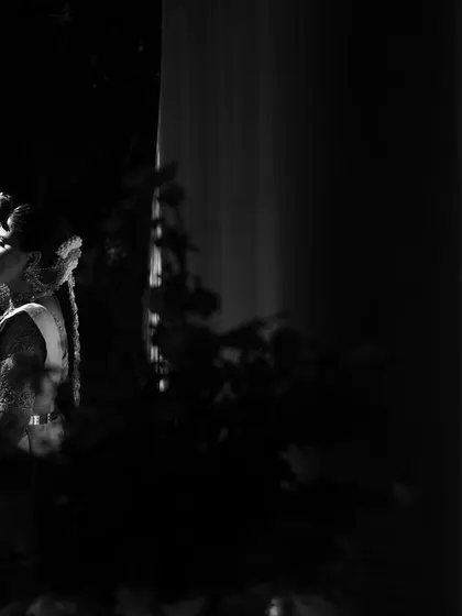 A high-contrast black and white portrait. The bride is caught in a sliver of light, creating a dramatic and artistic image that focuses on her form and emotion.