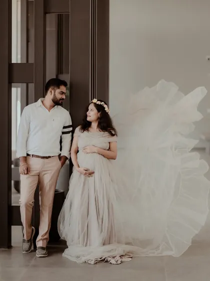 A beautiful indoor maternity portrait of a couple. The mother-to-be's ethereal gown flows out to the side, creating a sense of movement and elegance in this stylized pregnancy photo.