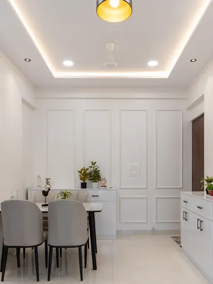 An elegant, all-white dining room where classic wall moulding adds texture and character. The simple furniture and focused lighting create a serene and sophisticated atmosphere.