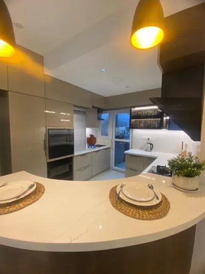 This kitchen features a breakfast bar with stylish pendant lights, creating a casual dining spot. The glossy cabinets and built-in oven add to the modern and streamlined feel.