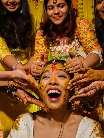 A close-up of pure laughter as the bride's friends playfully apply haldi to her face.