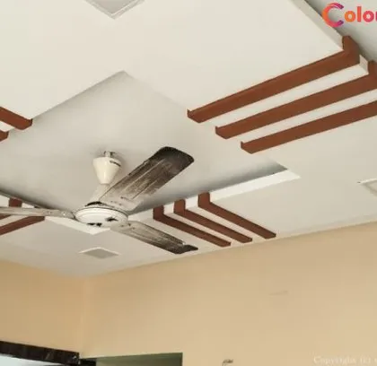 This design combines a clean white gypsum board with decorative wooden-finish beams. This approach adds warmth and a touch of classic elegance to the modern structure, perfectly integrating the ceiling fan into the central recessed area.