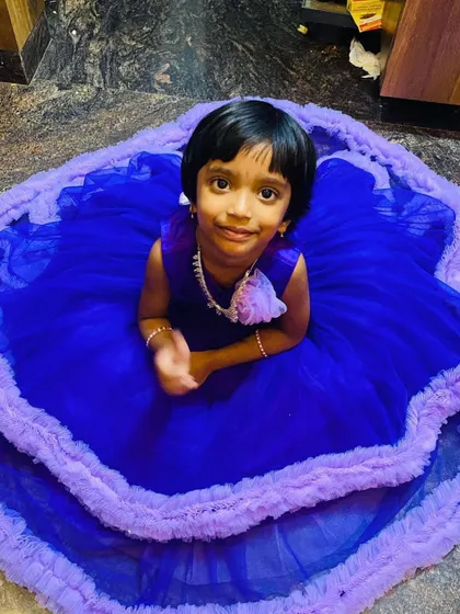 This little girl is sitting in her royal blue and lilac gown, which has a full, layered skirt.