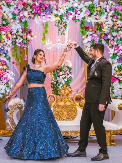 A beautiful couple portrait from the reception. The bride's one-shoulder blue lehenga and glamorous makeup look absolutely stunning under the floral decor.