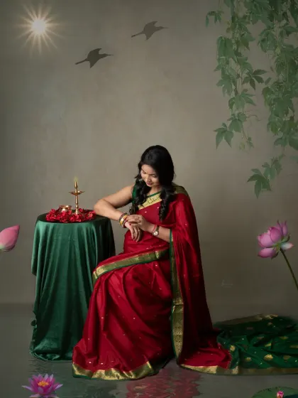 An artistic and symbolic portrait. The mom-to-be sits by a table with a lit diya, representing light and life, while wearing a beautiful red saree.