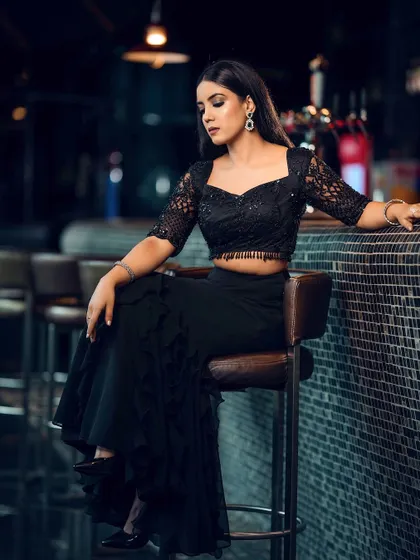 A full-length shot of the black ruffled skirt and lace crop top, showing the complete silhouette in a chic, dimly lit bar setting.