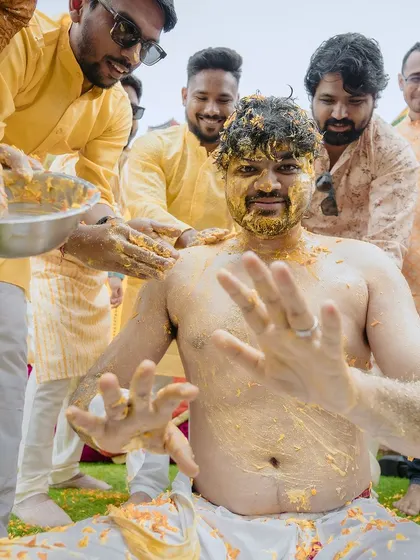 The groom's friends playfully covering him in haldi. This action shot is full of energy and laughter, capturing the true spirit of the ceremony.