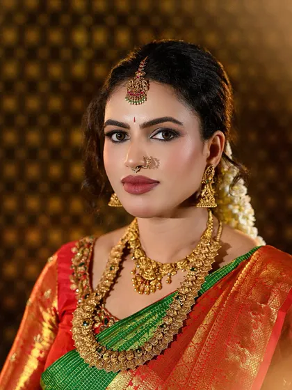 A complete look at a traditional South Indian bride in a stunning green and red Kanjivaram silk saree. The makeup features defined eyes, a bold matte lip, and a flawless base that complements the antique gold jewelry.