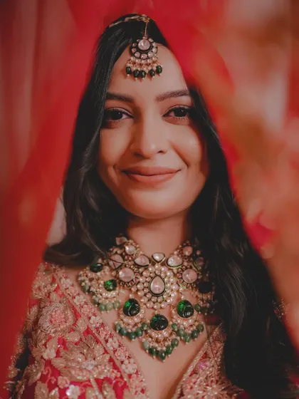 The bride's smile shines through her veil. This portrait highlights Priyanka's beautiful smile and her stunning emerald green jewelry.
