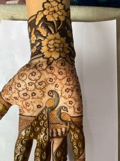 A stunning design featuring two peacocks on the back of the hand, surrounded by delicate floral patterns. This is a great example of modern mehandi art.