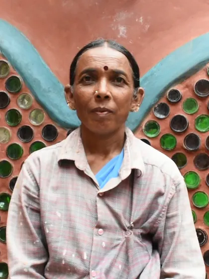 Portrait of Nagina, a patient and wise woman mason, in front of a colorful bottle wall. Her careful work is essential to creating these beautiful, functional features.