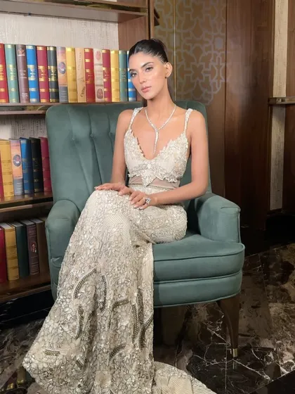 The model seated, looking elegant and poised with her sleek ponytail and glamorous cocktail dress.