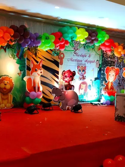 A vibrant jungle theme stage setup with a colorful balloon arch, animal cutouts, and light-up marquee letters.