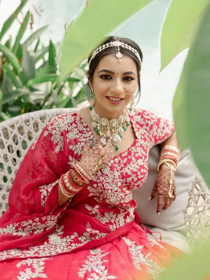 A beautiful portrait of the bride seated, looking serene and happy. The makeup is flawless, and her red lehenga looks absolutely stunning.