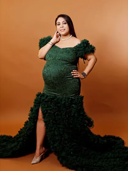 A glamorous full-length portrait of a mother-to-be in a dark green ruffled gown, showcasing its texture and trail in our studio.