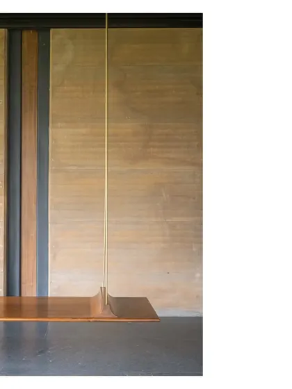 A minimalist swing at the Lakeshore house, where a simple wooden seat is suspended by a slender brass rod against a wall of rammed earth. Details like these are what turn a building into art.