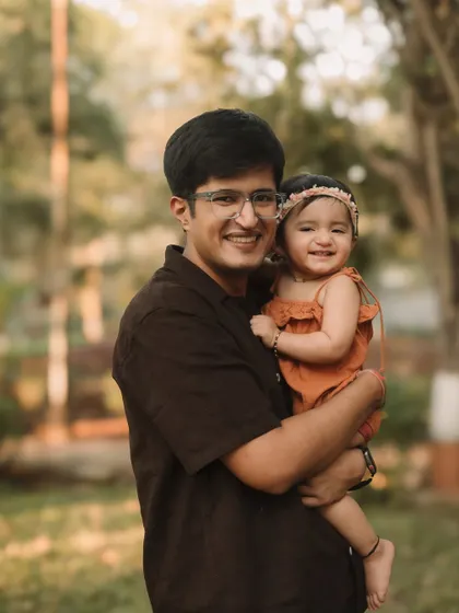 A proud father holds his smiling daughter during their golden-hour outdoor photoshoot.