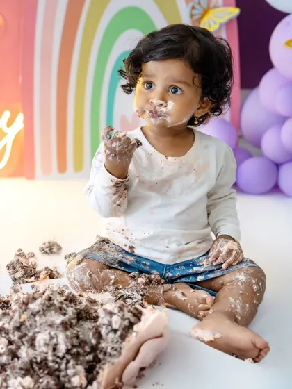 A full-on messy cake smash! This little one is having a blast, and her happy, cake-covered face says it all.