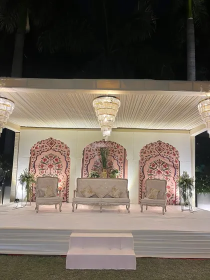 A Sufi-inspired stage setup with delicate arches, traditional patterns, and elegant white seating, all illuminated by the soft glow of tiered chandeliers.