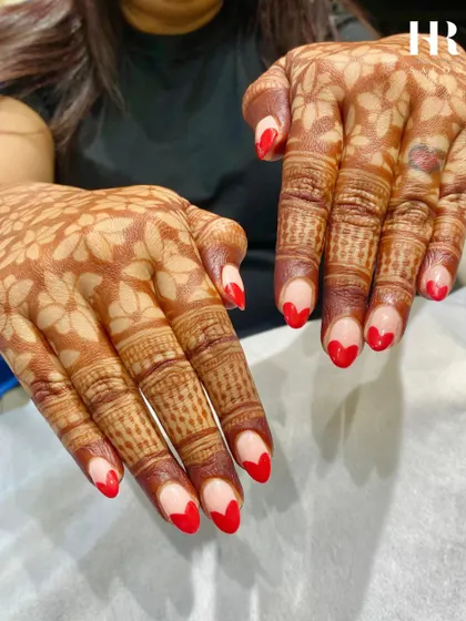 We love creating nail art that complements your special occasions. Here, we designed a modern French manicure with vibrant red heart-shaped tips to perfectly match this client's beautiful mehendi.