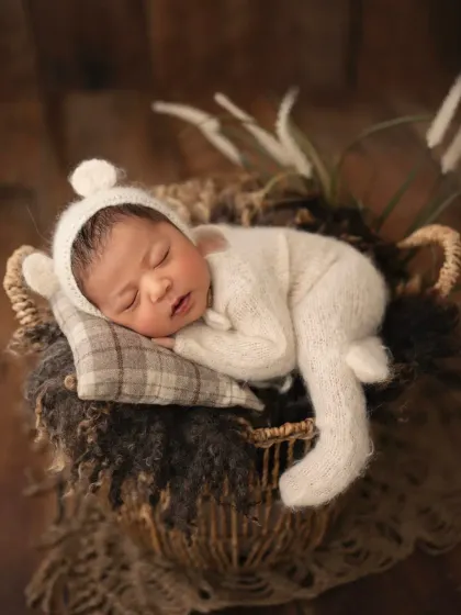Dressed in a fuzzy bear romper, this newborn is sleeping peacefully in a prop basket. The textures and earthy tones create a warm and cozy feel.