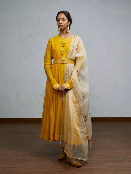 A graceful, full-length shot of a yellow anarkali suit. The model's poised stance and the clean studio background make this a perfect image for a lookbook, highlighting the elegance and traditional design of the outfit.