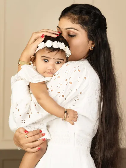 A mother's gentle kiss on her baby's forehead. This close-up shot, with both in white, is a pure and simple expression of a mother's love.