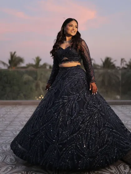 A full-length shot against a sunset sky. The deep blue of her lehenga and the pop of blue on her eyes create a stunning, cohesive look.