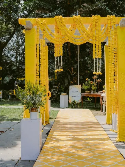 A bright and sunny Haldi entrance with a yellow patterned aisle runner and a marigold-draped archway.