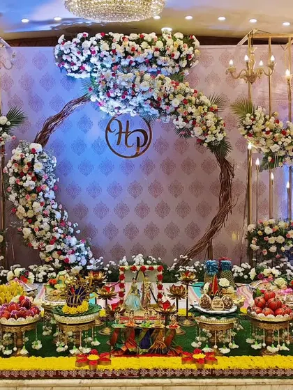 A beautiful engagement stage with a floral wreath monogram, chandeliers, and a full display of traditional offering plates.