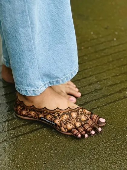 A simple and elegant floral mehandi for the feet, shown against a wet surface. This artistic shot highlights the beauty and durability of our designs.
