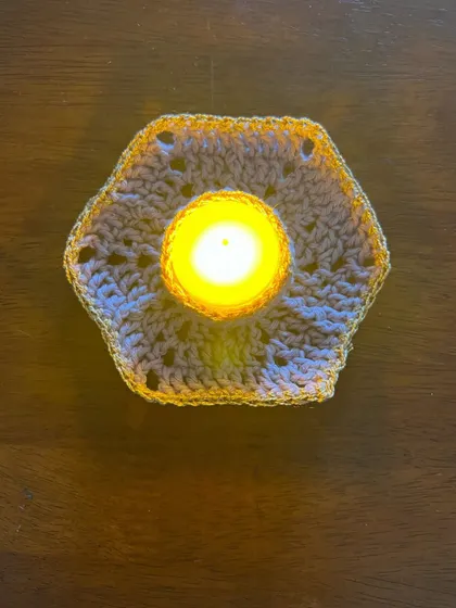 A top-down view of the hexagonal tealight holder, showing the intricate crochet pattern. The golden yarn border adds an extra festive sparkle when it catches the light.