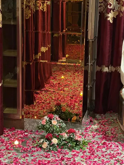 A detail shot of the 'Welcome Bride' room, showing a mirrored wardrobe reflecting the floor covered in red rose petals and candles.
