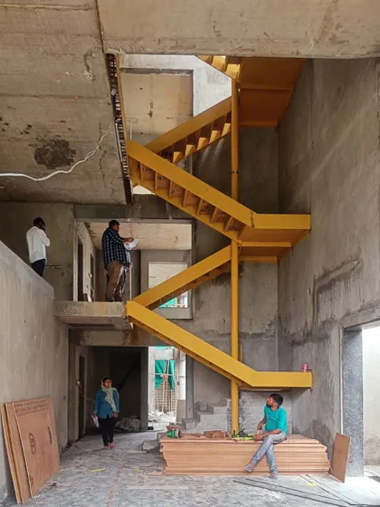 A vibrant yellow metal staircase is installed during the construction of the Jayanagar Residence. This image captures a key moment in the building process, showing how a bold design element begins to define the character of the interior space.
