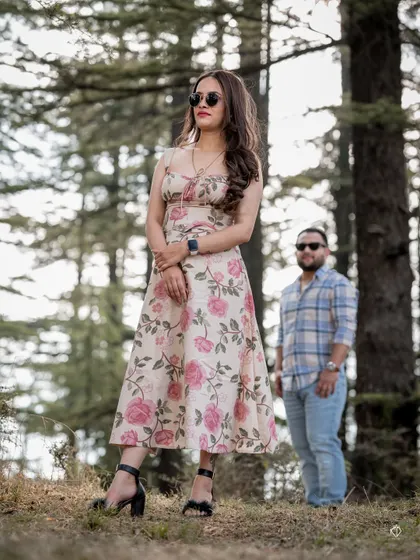 A stylish portrait of the woman in a floral dress, posing in the forest with her partner in the background. This shot has a fashionable, editorial feel.