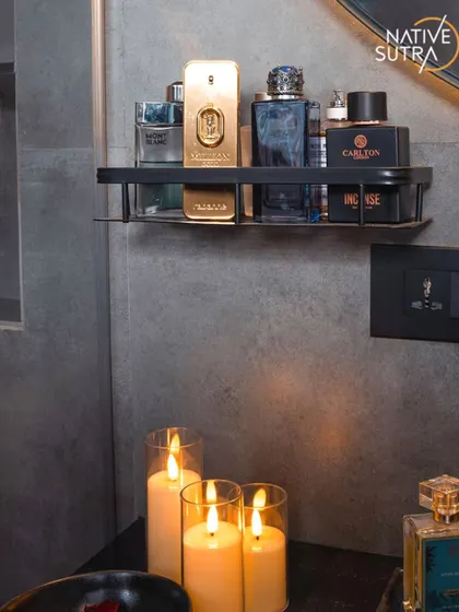 A detail shot showcasing the styling in the moody bathroom. A collection of high-end colognes on a black shelf and the warm glow of candles add a layer of personal luxury and ambiance.