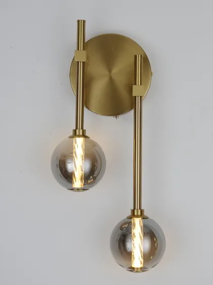 A modern wall sconce with two smoked glass globes on a brass fixture. A stylish choice for a bedroom or living area.