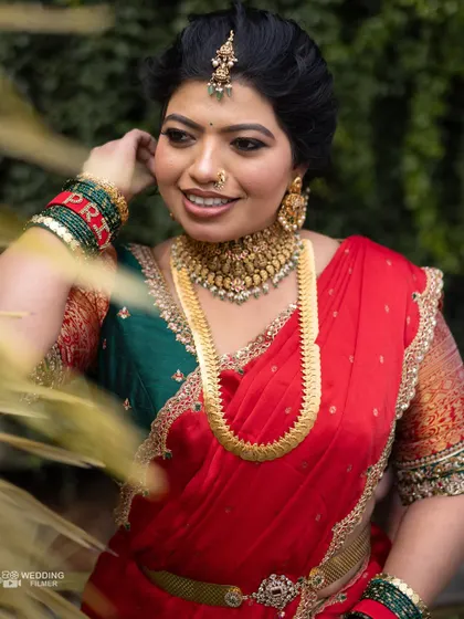 A radiant portrait of a South Indian bride in a classic red and green saree, her smile lighting up the frame.