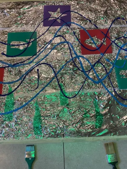 A simple setup for exploring art and reflection. Foil on the floor with stencils and paint invites children to see how light and color interact on a shiny surface, creating a dynamic and engaging art experience.