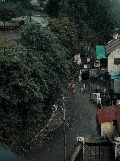 A high-angle shot of a person walking down a wet street in Mussoorie. The rain adds a dynamic and moody element to the scene.